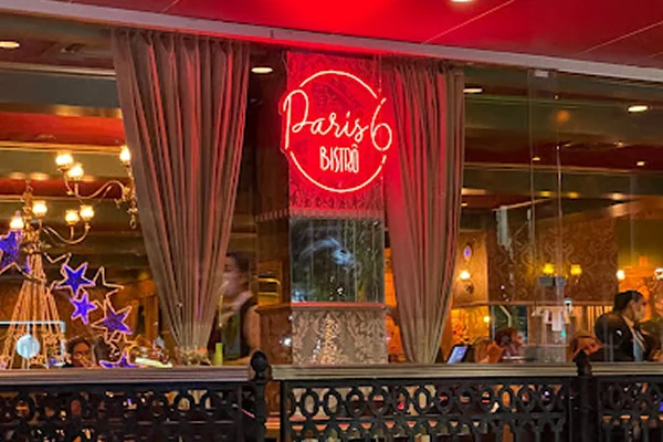 Fachada do Paris 6 Bistrô com cortinas e uma placa de néon vermelha, criando um ambiente clássico e acolhedor.