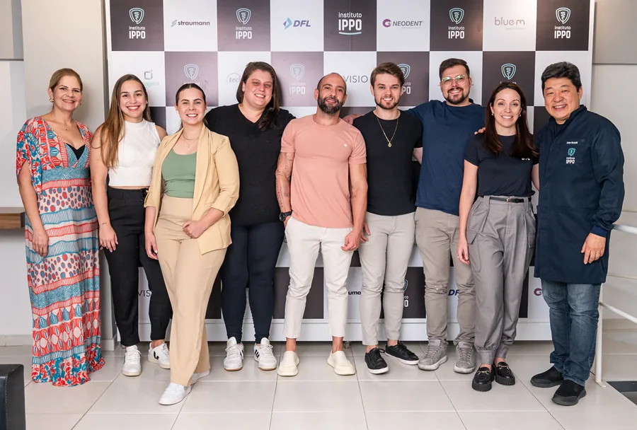 Grupo de estudantes e professores posando juntos em frente ao painel de patrocinadores no Instituto IPPO, celebrando o término de um módulo da especialização.