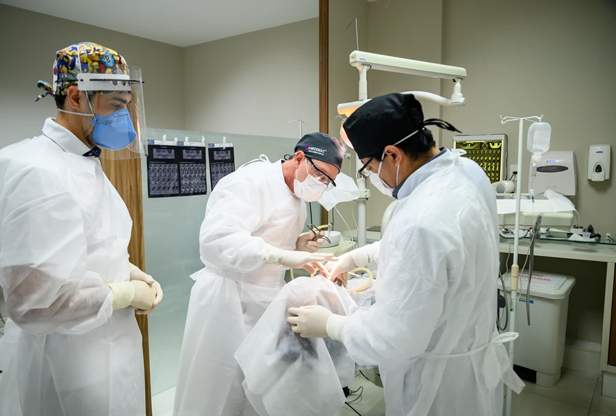 Procedimento clínico sendo realizado por dentistas e alunos, todos usando trajes de proteção, durante uma aula prática no Instituto IPPO.
