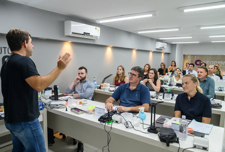 Instrutor de odontologia explicando um conceito para alunos em uma sala de aula com projetor, com participantes atentos.
