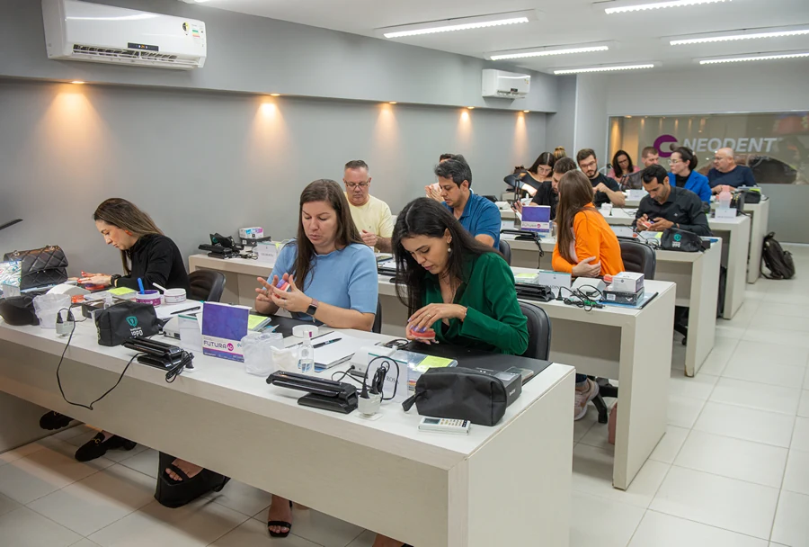 Alunos em sala de aula realizando atividades práticas, com equipamentos odontológicos e materiais sobre as mesas.