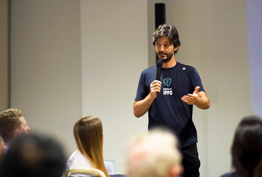 Palestrante do Instituto IPPO com microfone, realizando uma apresentação para um grupo de participantes.