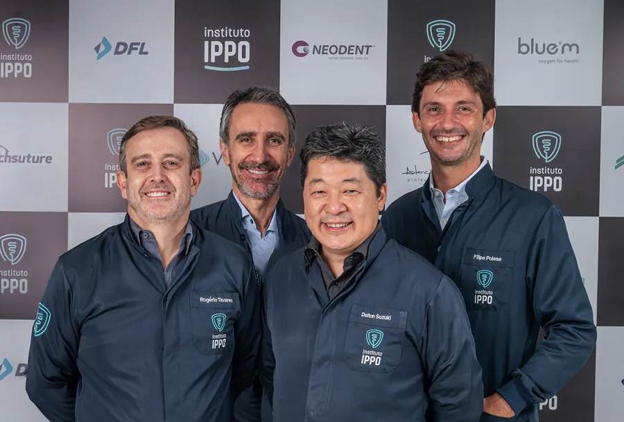 Foto de quatro profissionais do Instituto IPPO sorrindo em frente a uma parede com logotipos de patrocinadores.