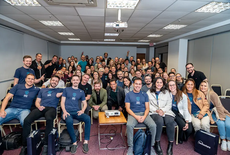 Foto em grupo dos participantes de um evento do Instituto IPPO, todos sorrindo e olhando para a câmera em uma sala de conferências.