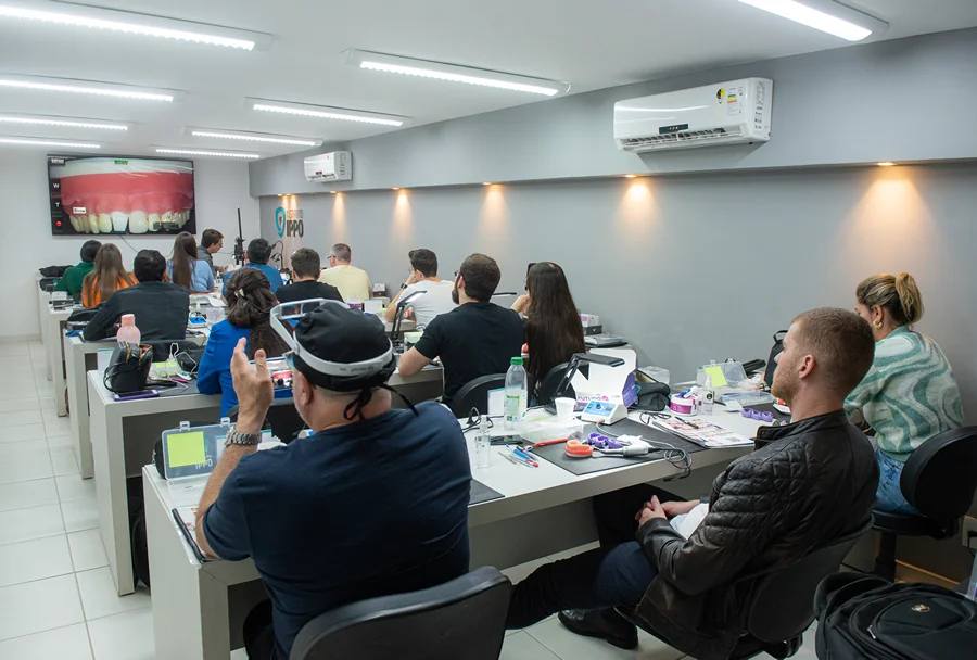 Alunos assistem a uma apresentação sobre dentição exibida em uma tela grande, em uma sala de aula moderna no Instituto IPPO.
