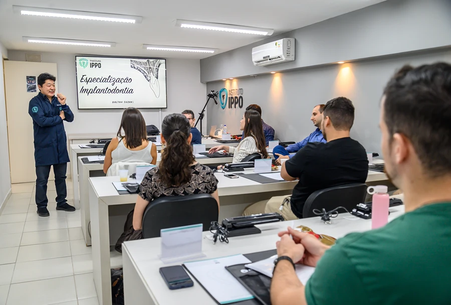O Dr. Dalton Suzuki ministra uma aula sobre especialização em implantodontia, com alunos participando em uma sala do Instituto IPPO.