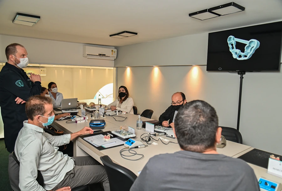 Instrutor utilizando um telão com imagem de modelagem 3D para explicar técnicas de cirurgia guiada aos alunos.