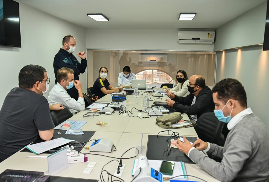 Instrutor e participantes em uma mesa redonda, conversando e trocando ideias enquanto analisam informações exibidas em um laptop.