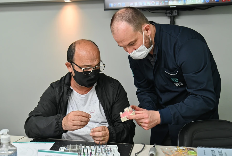 Instrutor do Instituto IPPO mostrando um detalhe técnico para um dos participantes, com ambos usando máscara.